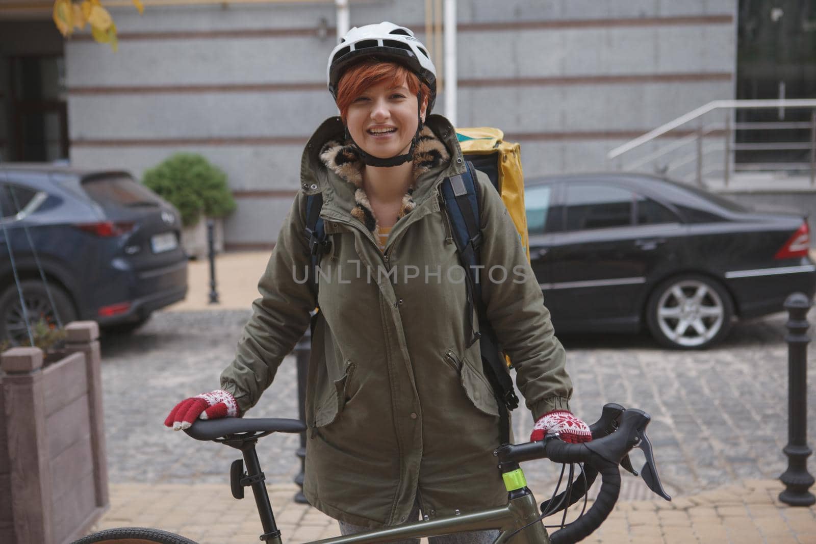 Happy young woman working in delivery service as courier, standing with her bike outdoors