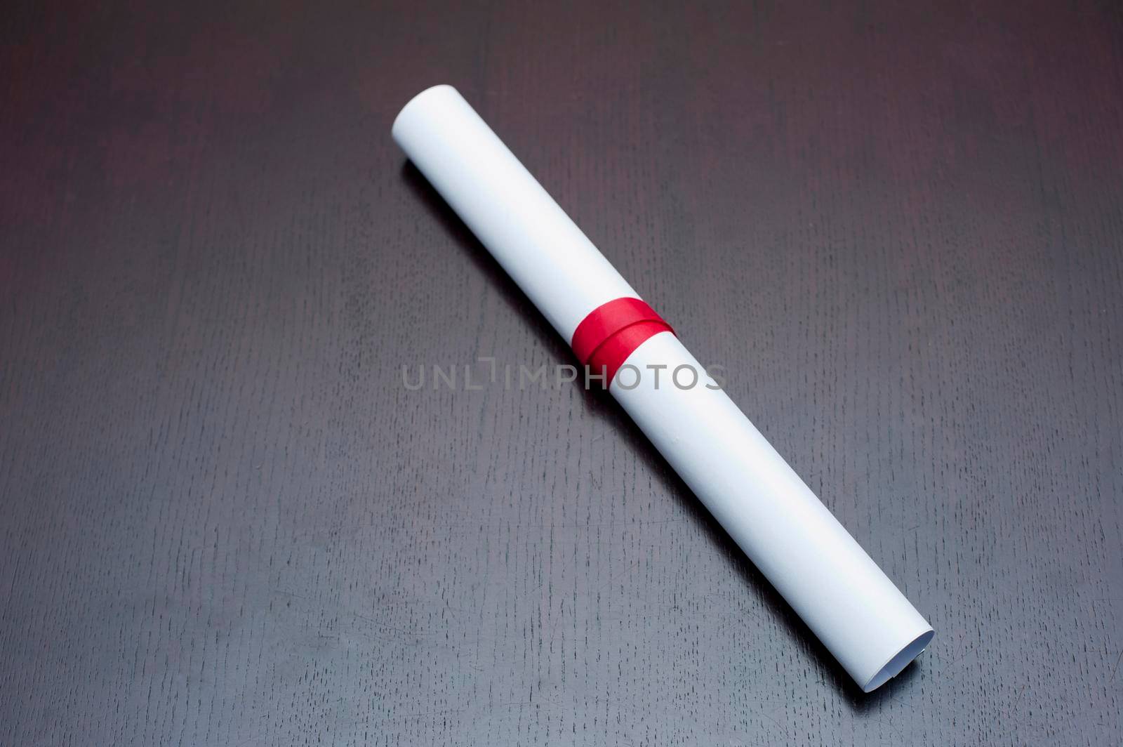 Educational background of a rolled graduation certificate tied with a red ribbon lying on a grey background with copysapce