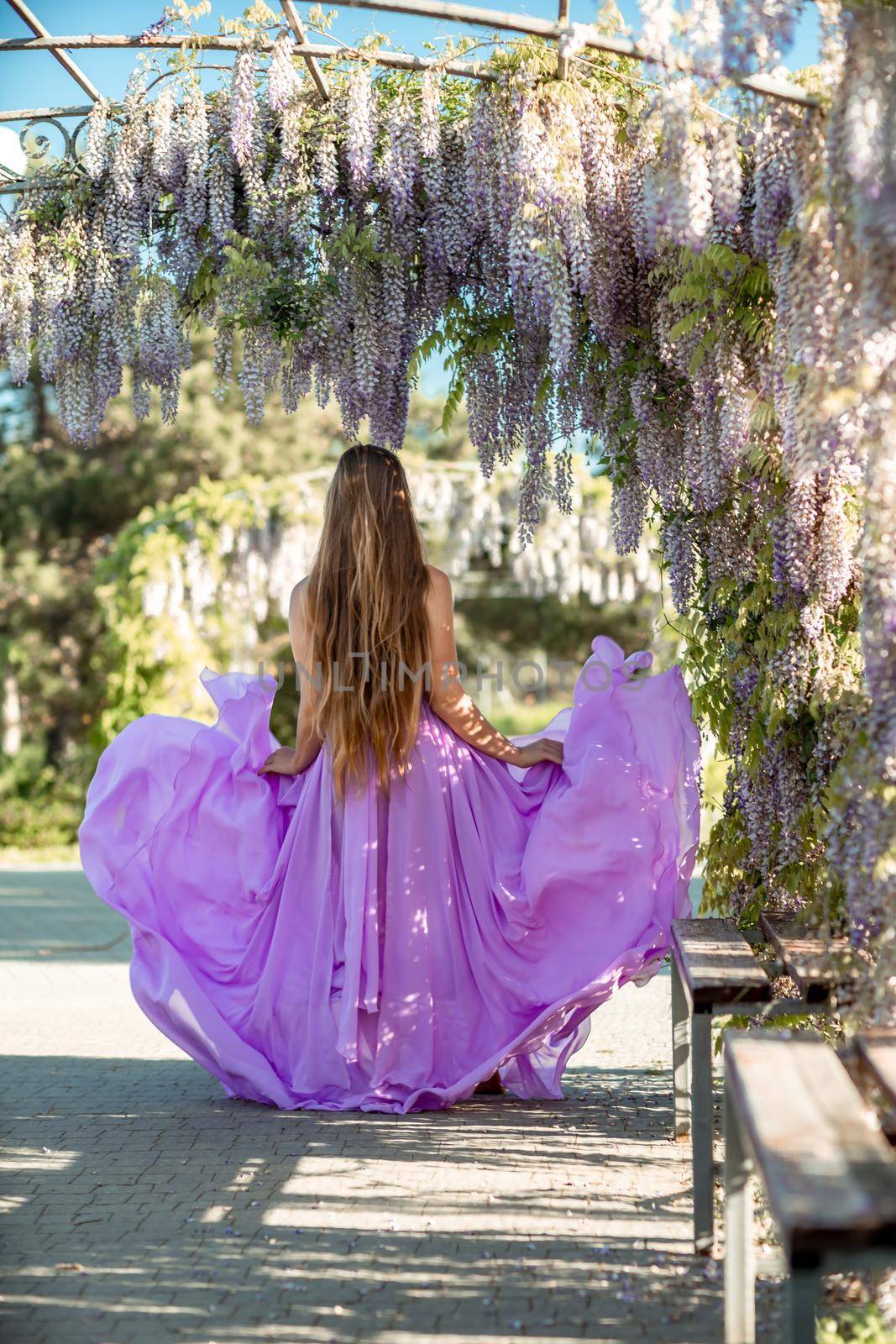 Thoughtful happy mature woman surrounded by chinese wisteria in purple dress by Matiunina