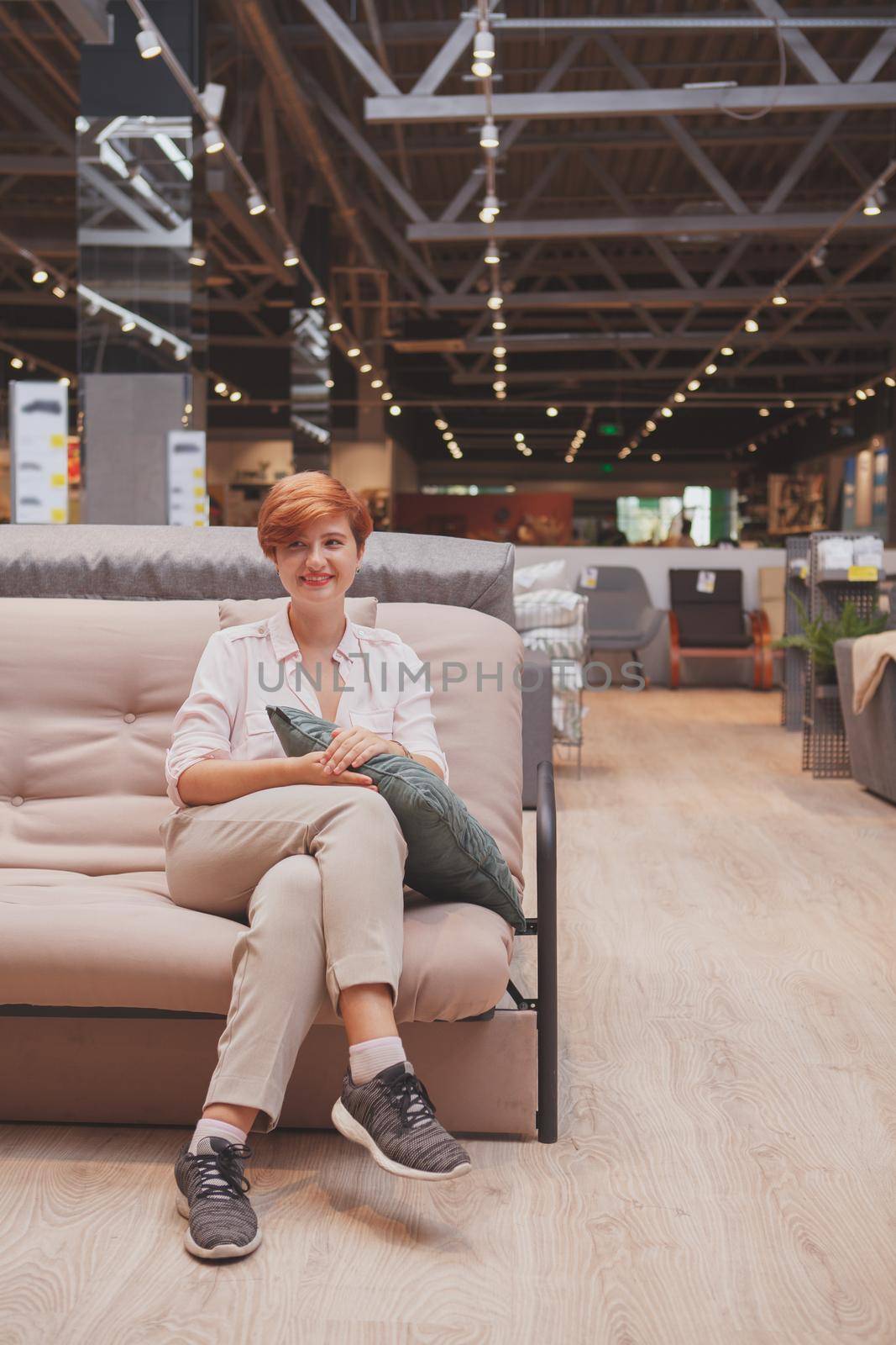 Vertical shot of a cheerful female customer sitting on a new couch at furniture store