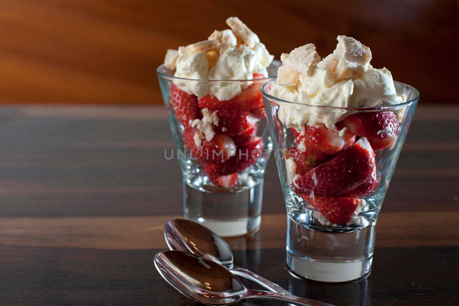 Delicious fresh ripe red strawberries and whipped cream dessert served in two sundae glasses on a wooden counter with copyspace