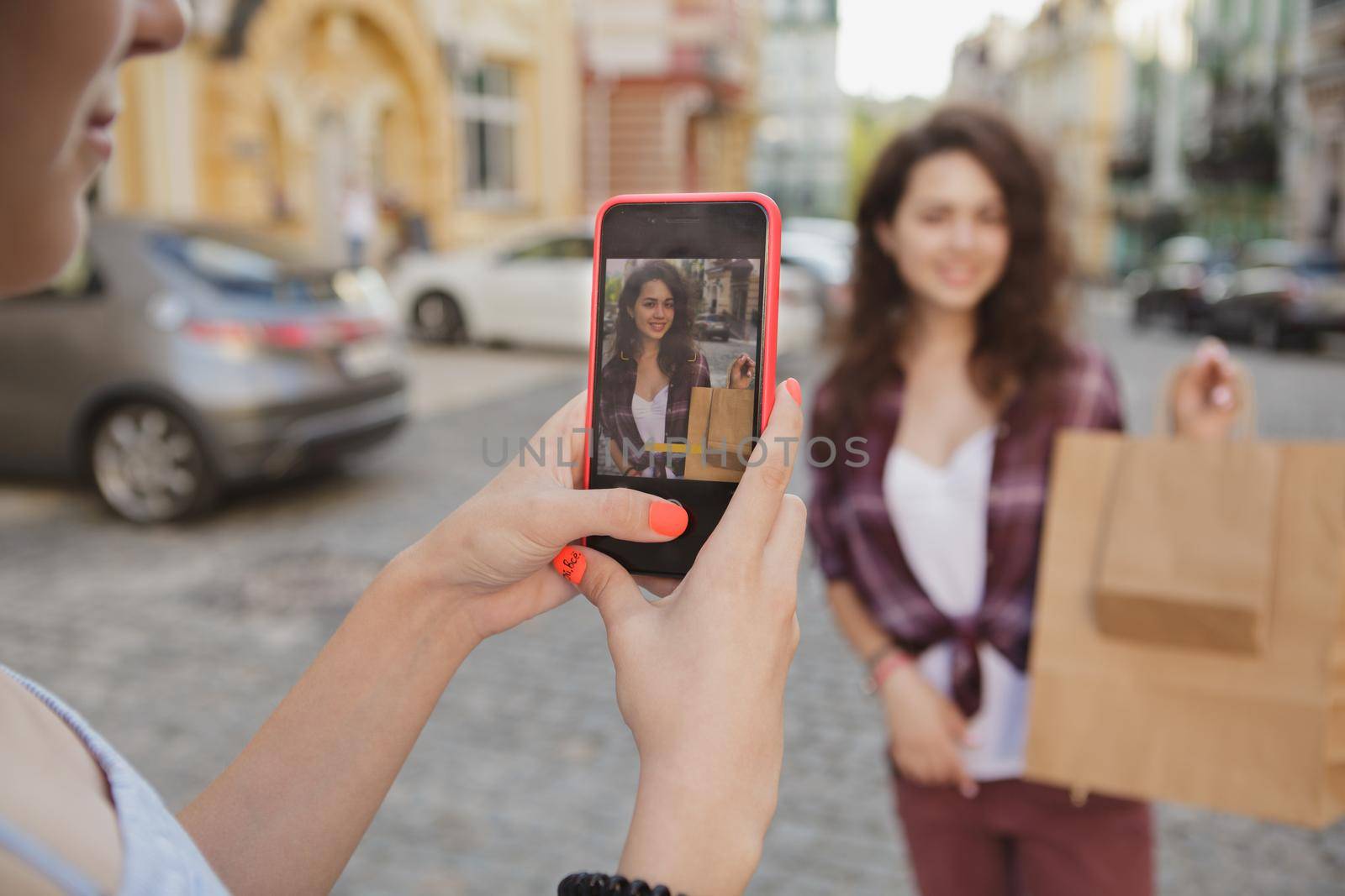 Cropped close up of a smart phone in the hands of a woman taking photo of her friend on the city streets. Female friends enjoying sightseeing and taking photos after shopping