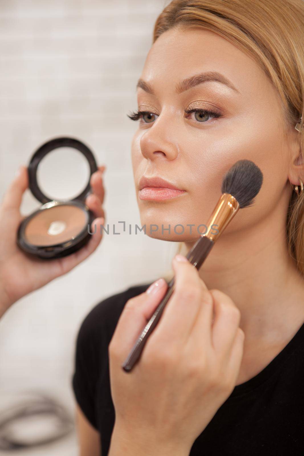 Vertical close up of a beautiful woman getting professional makeup by beautician at the salon