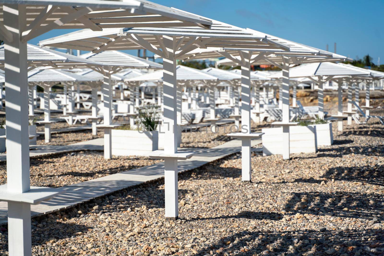 Rows of wooden umbrellas from the sun on the seashore in the morning. Wooden paths on the sand between umbrellas. Beach holiday at the resort