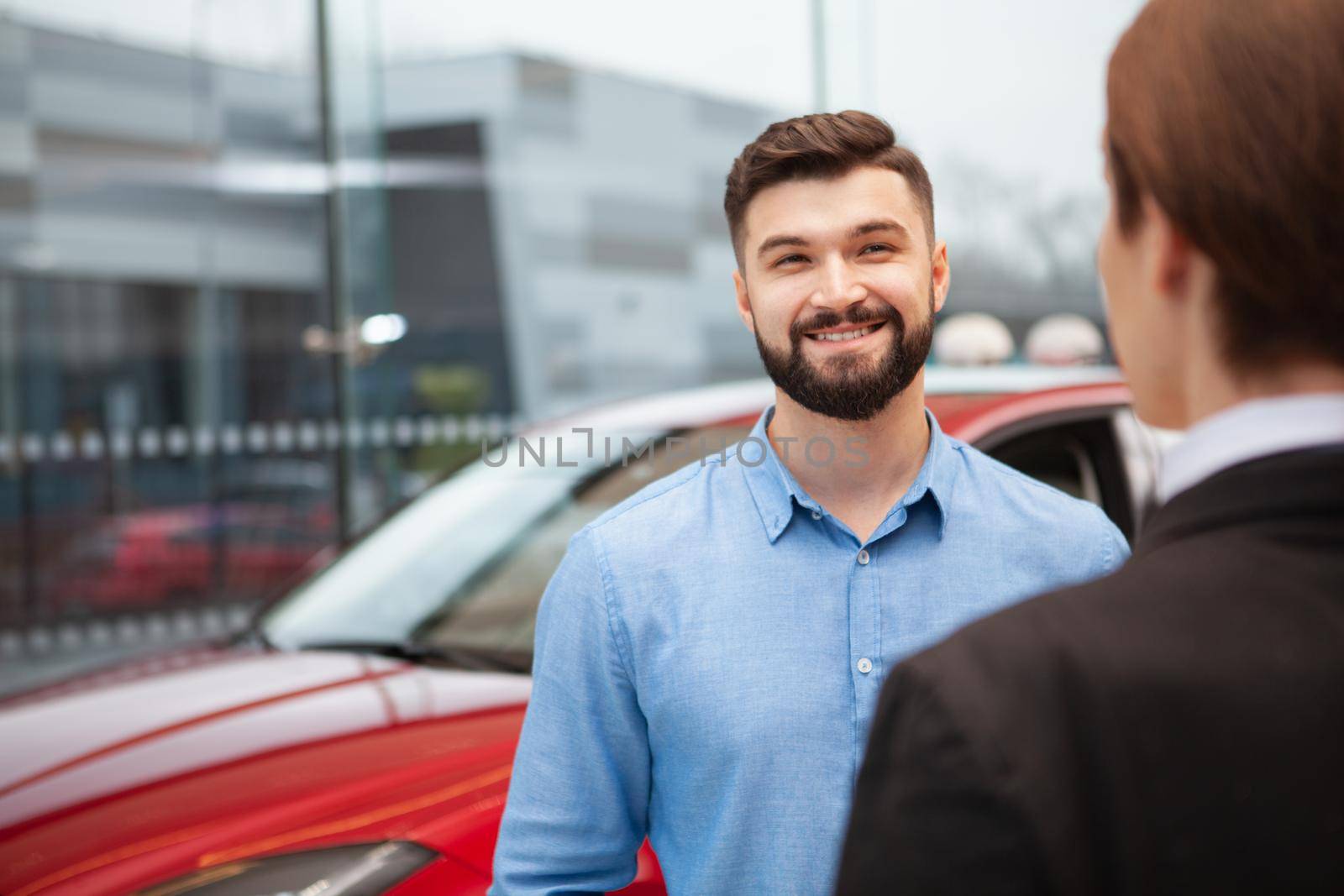 Cheerful handsome man smiling joyfully while talking to car dealership manager, buying new car, copy space