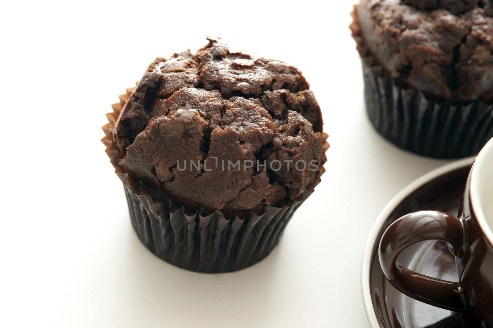 Tasty freshly baked double chocolate muffins next to cropped coffee cup on white table