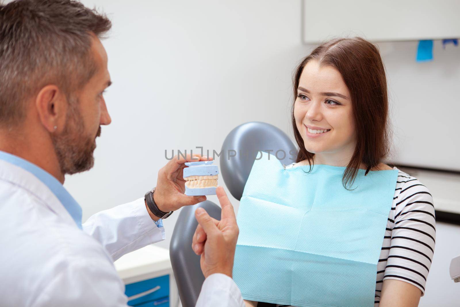 Beauitful cheerful young woman smiling at her dentist. Mature dentist talking to his lovely female patient