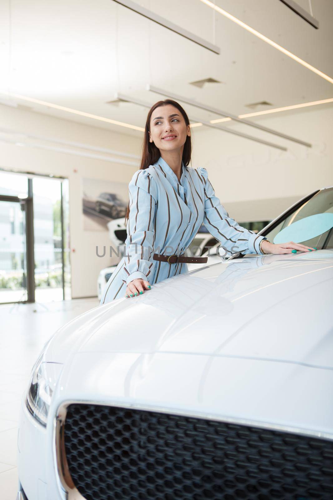 Vertical shot of a cheerful beautiful woman buying new car at the dealership