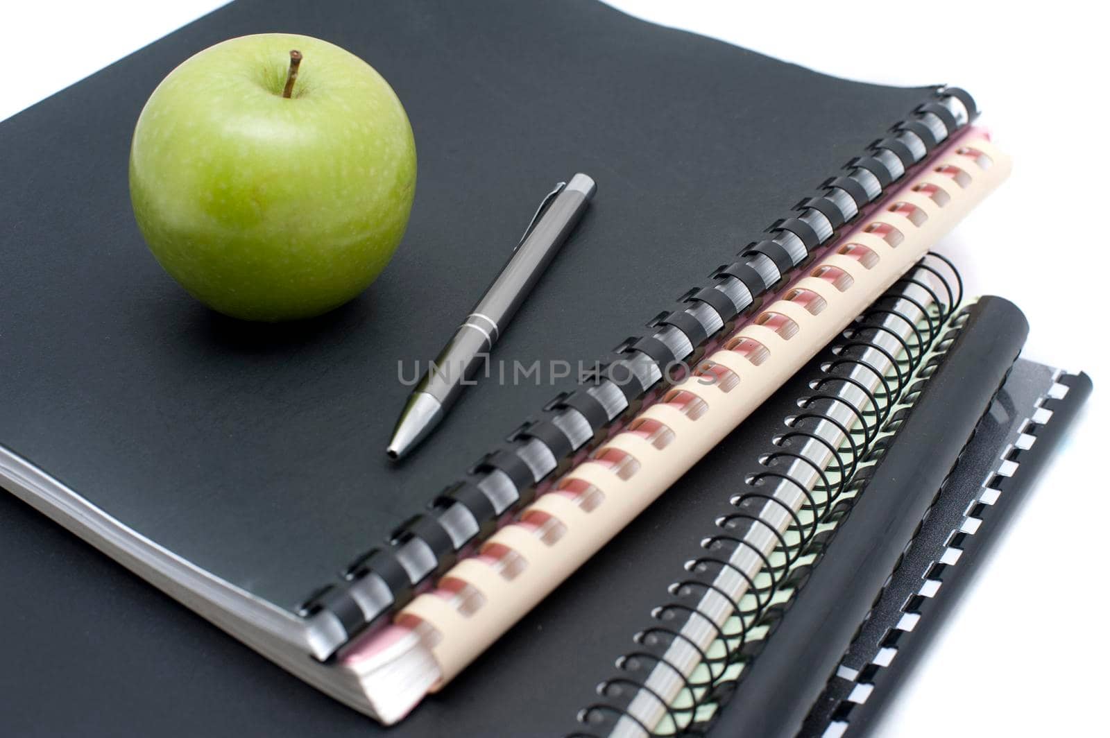 Spiral bound notebooks for taking university notes topped with a pen and fresh healthy green apple to eat as a snack while studying