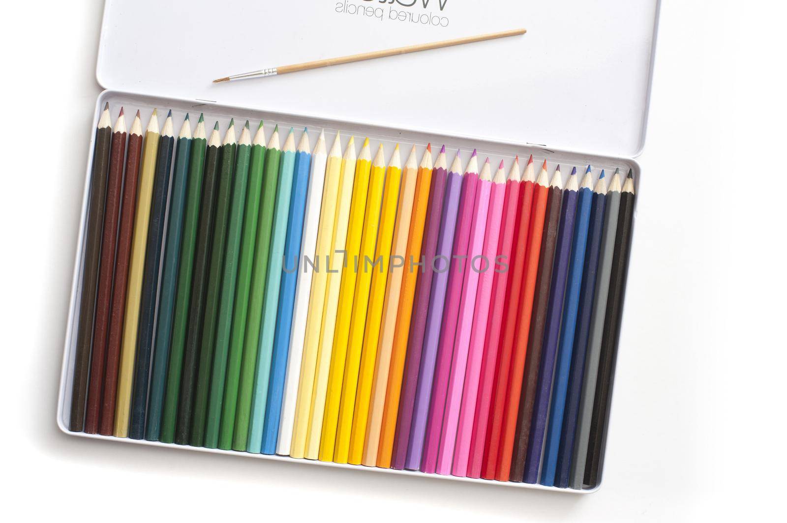 Angled top down view on open white tray full of various colored pencils and paintbrush over white background with slight drop shadow
