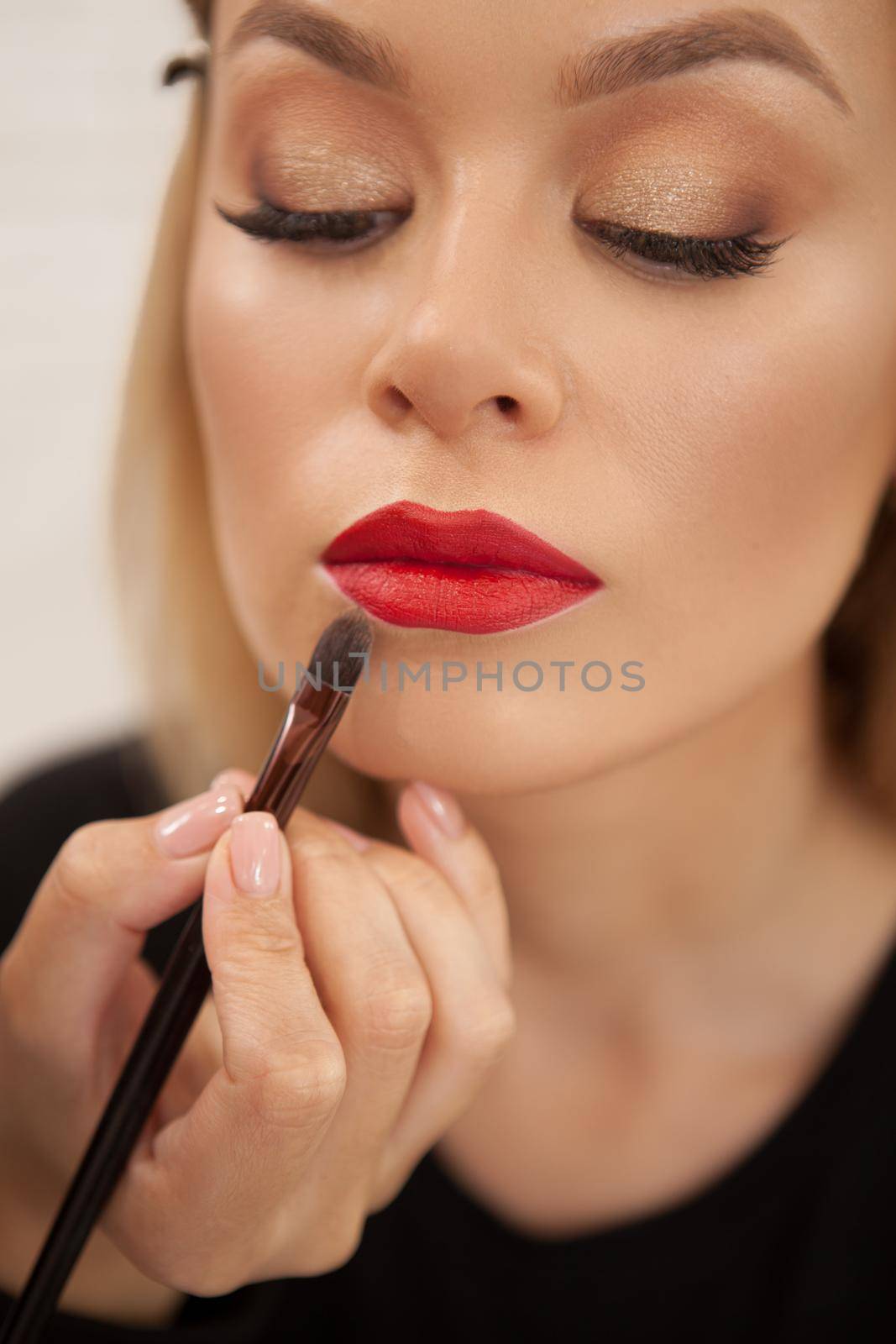 Vertical closeup of a beautiful woman having her lips painted with red lipstick