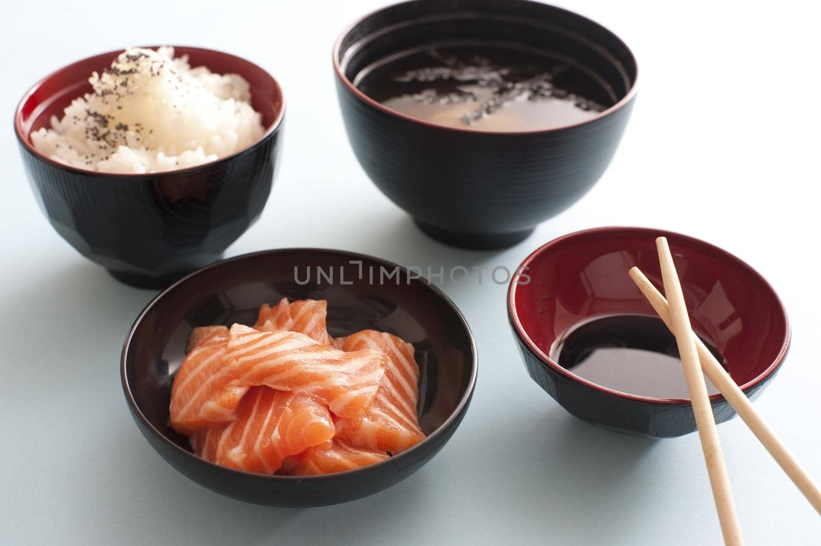 Raw salmon sashimi with soy sauce and a side dish of rice served with Asian chopsticks in individual bowls