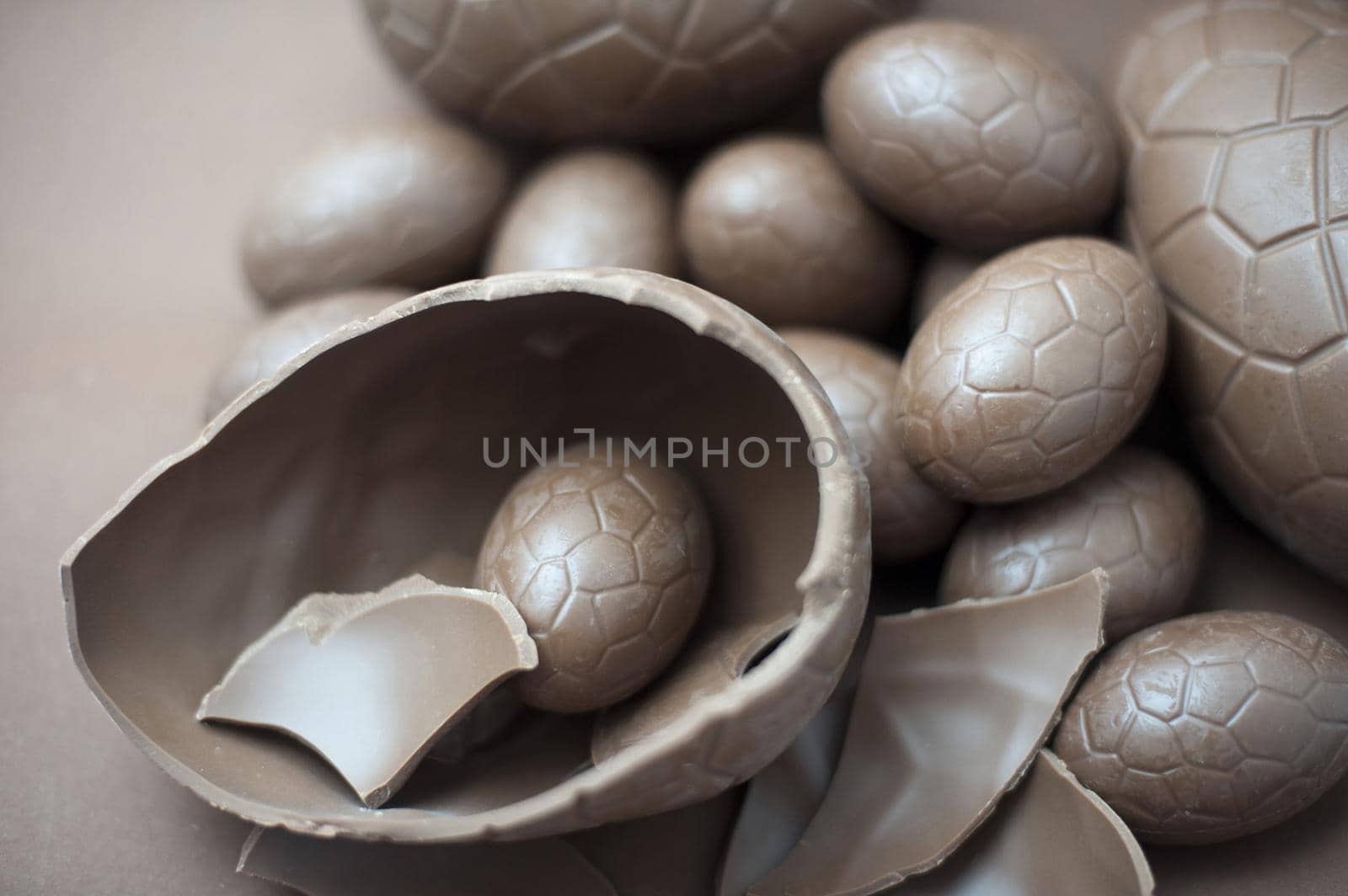Cracked milk chocolate Easter egg accompanied by a collection of various sized eggs on a brown background