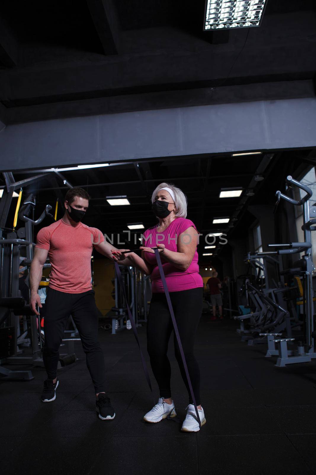 Vertical full length shot of a senior woman and her fintess coach wearing medical face masks at the gym