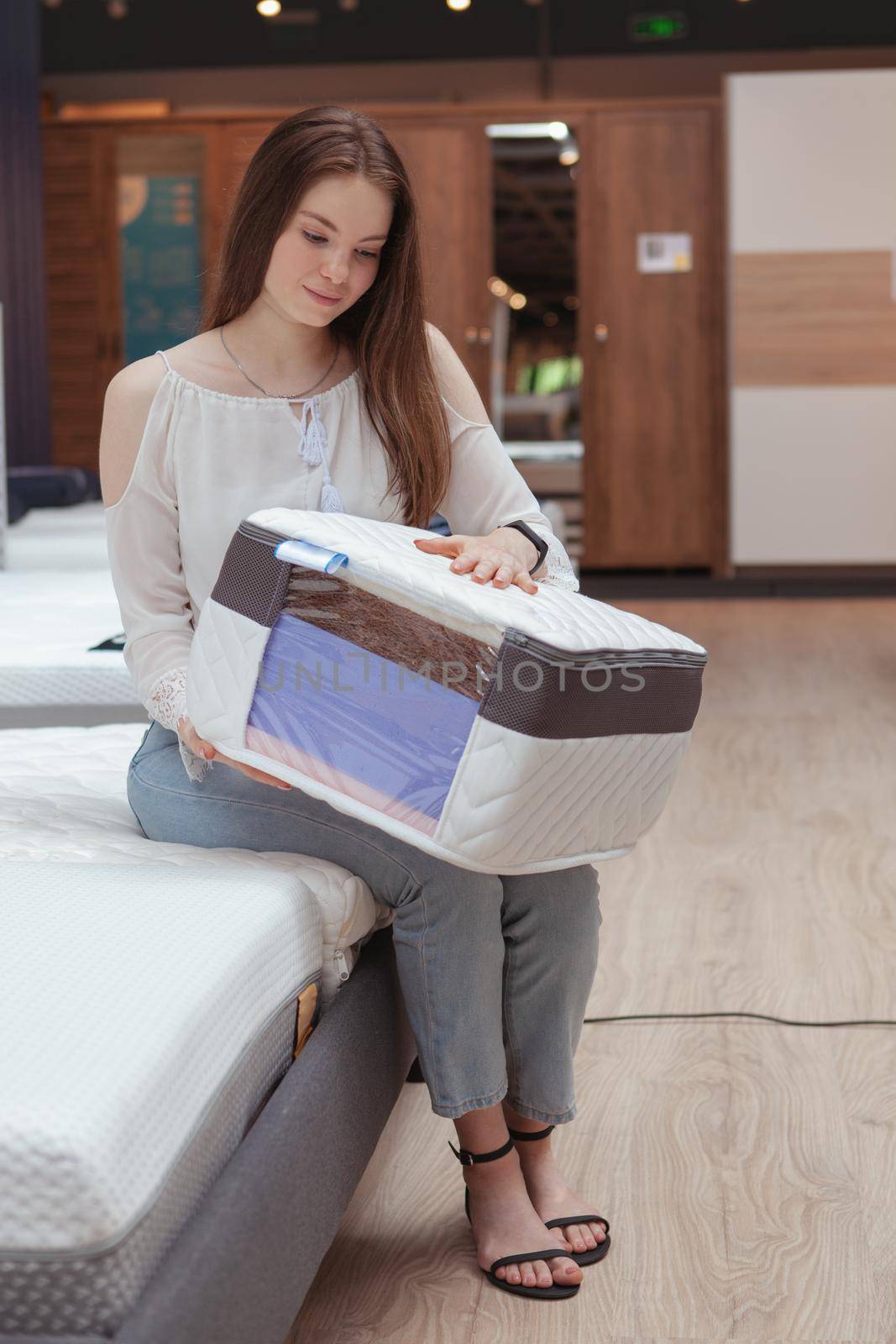 Vertical shot of a woman examining orthopedic mattress sample at furniture store