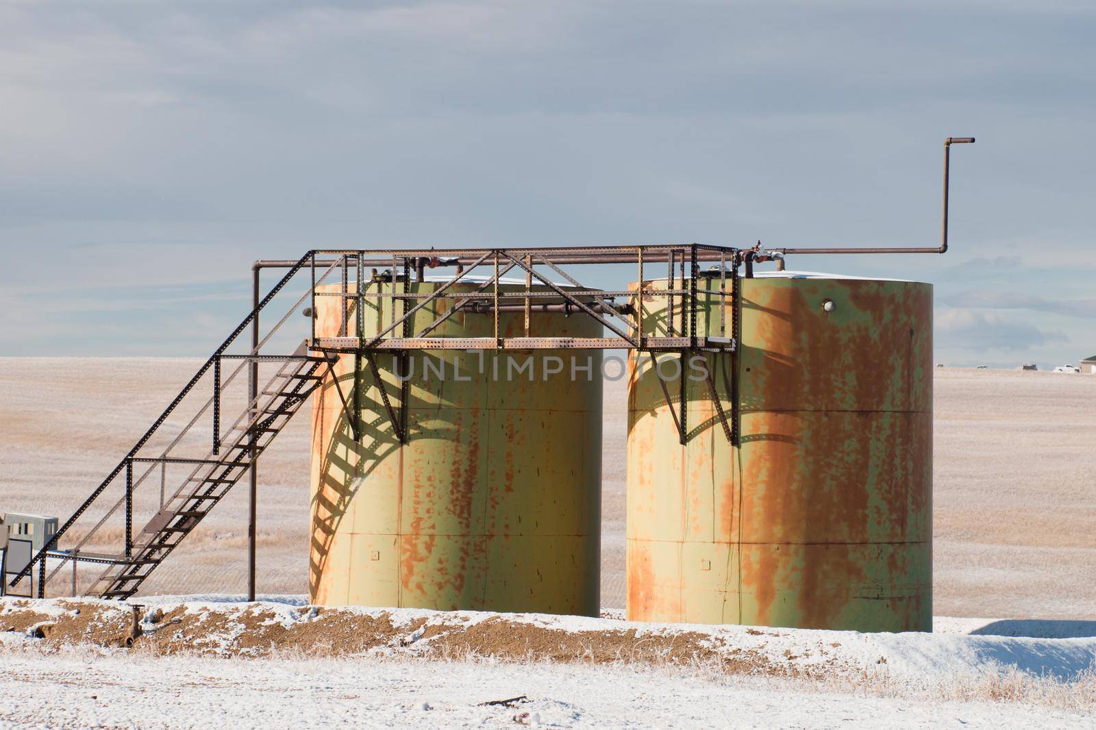Rusted industrial storage tanks in winter landscape.