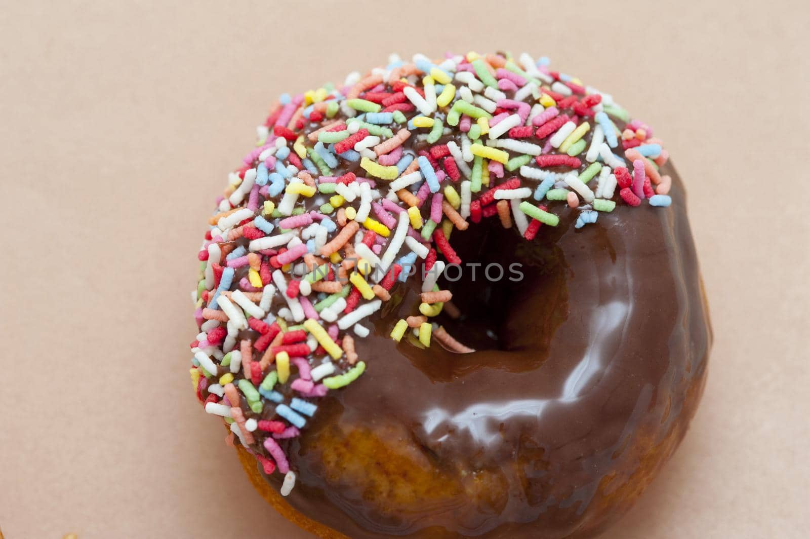 Delicious fresh chocolate ring donut with colorful sprinkles on a beige background with copyspace, overhead view