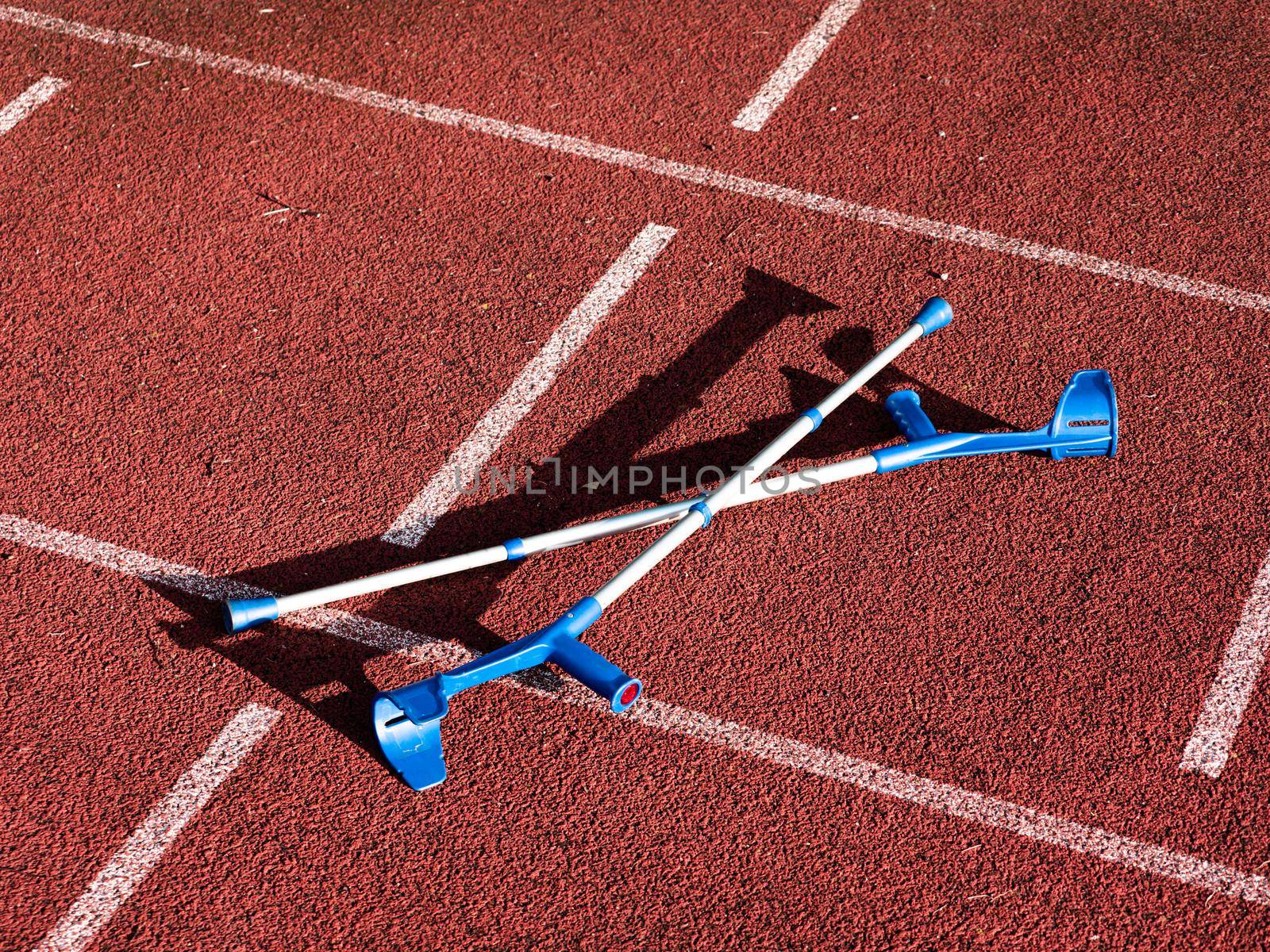 Forearm crutches on red running track on stadium. Run lines on front tracks 