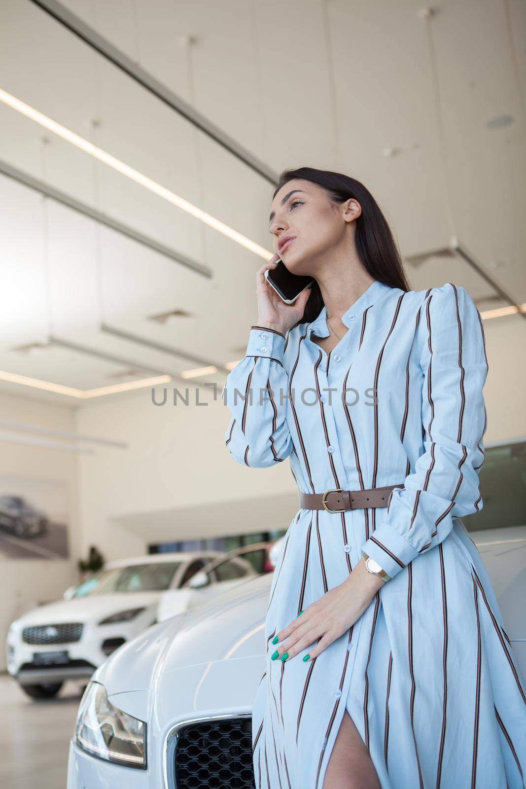 Vertical portrait of an elegant woman talking on her mobile phone at car dealership