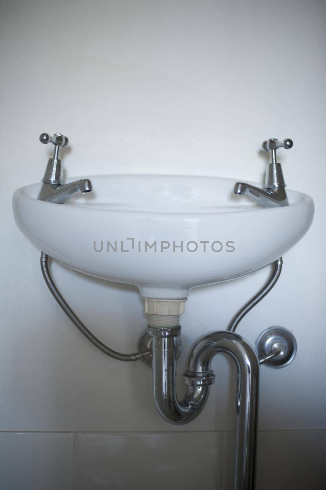 Simple ceramic white hand basin viewed low angle to show the pipes and plumbing mounted on a white wall in a restroom, or bathroom