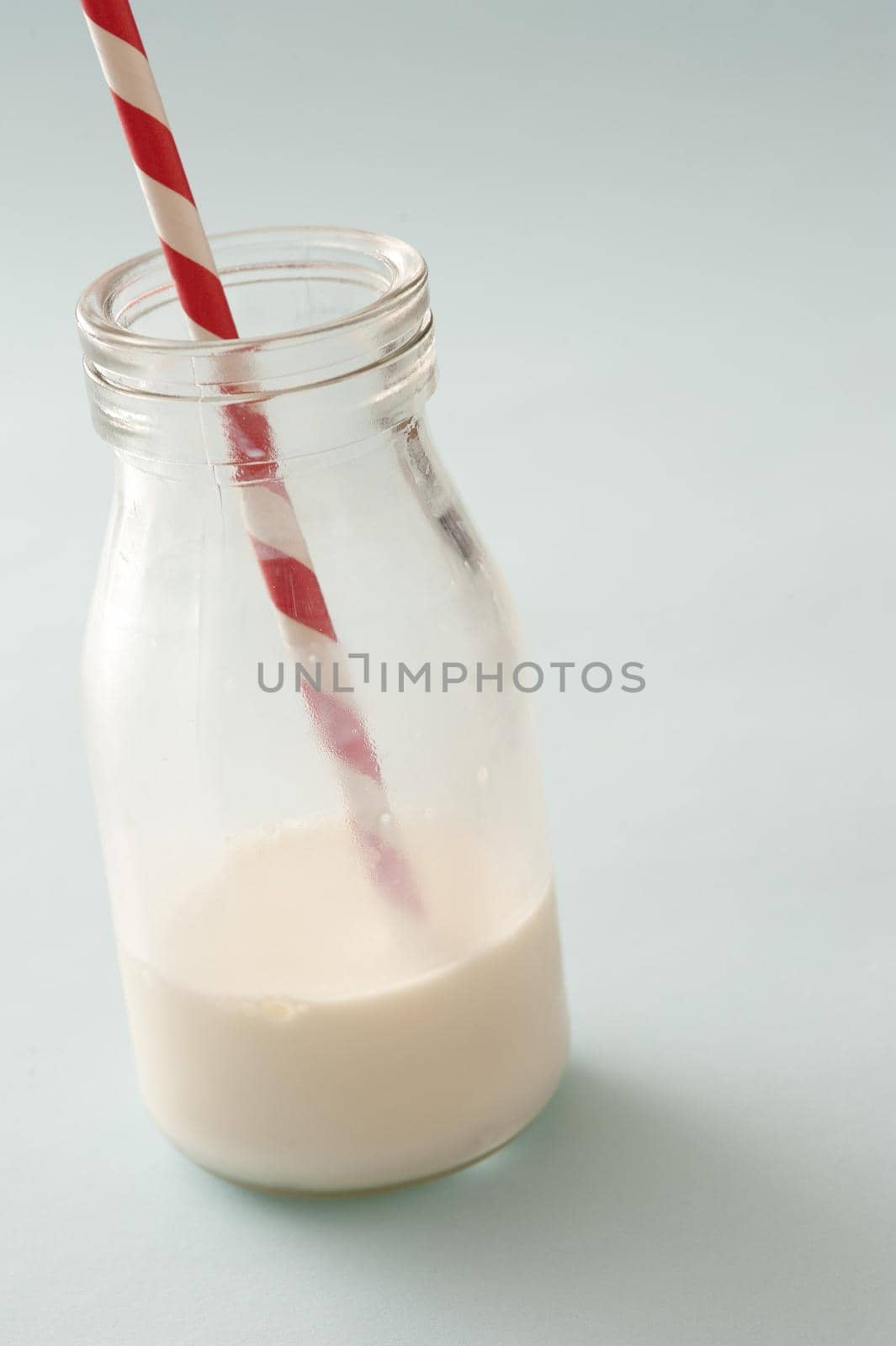 Small blank glass jar half full with whole milk and red and white straw over neutral background
