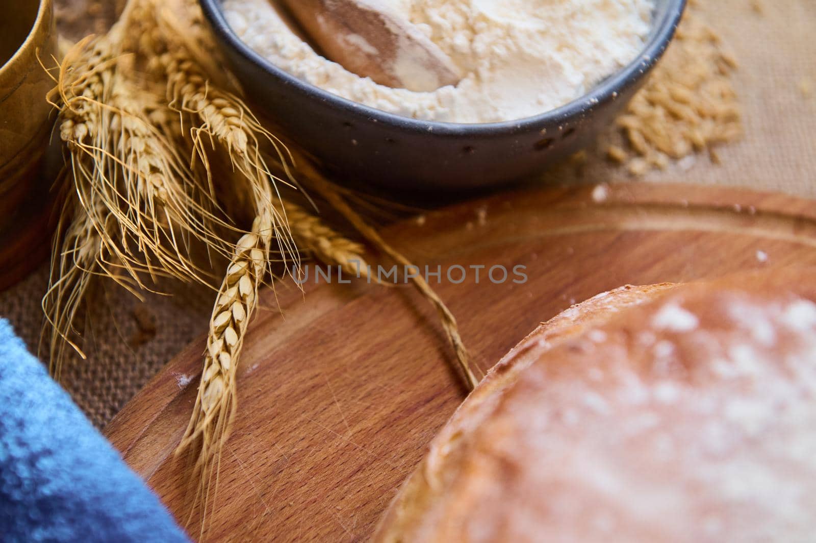 Soft focus on the spikelets of wheat next to a bowl with white flour and fresh baked whole grain bread on wooden board by artgf