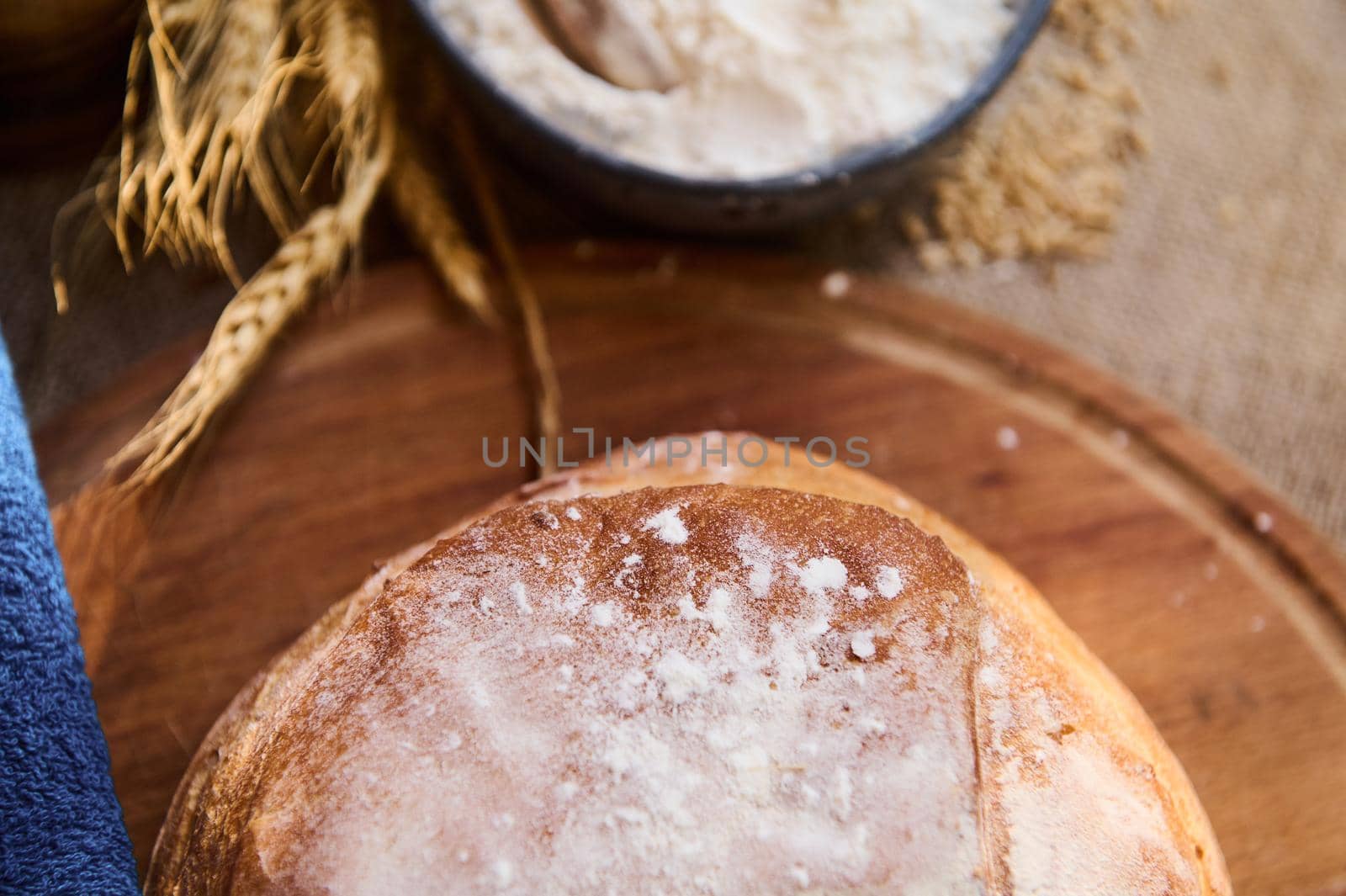 Cropped view. Still life. A loaf of sourdough bread with crust, on a wooden board, next to white flour and ears of wheat by artgf