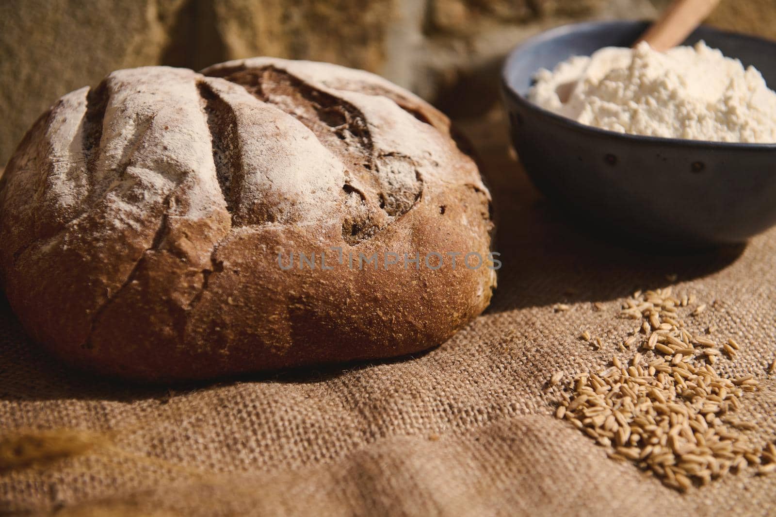 Still life with fresh baked sourdough wheaten bread, ears of wheat and baking ingredients on a burlap tablecloth by artgf