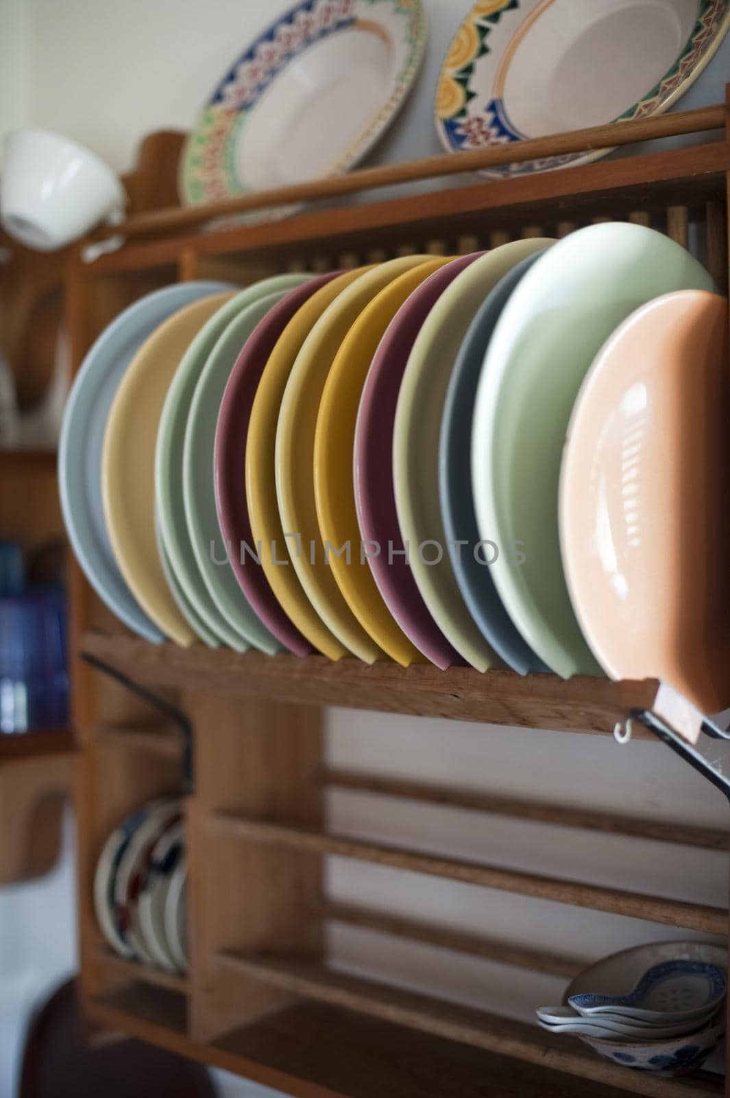 Colorful clean assorted ceramic plates in a wooden plate rack mounted on a kitchen wall in a close up view