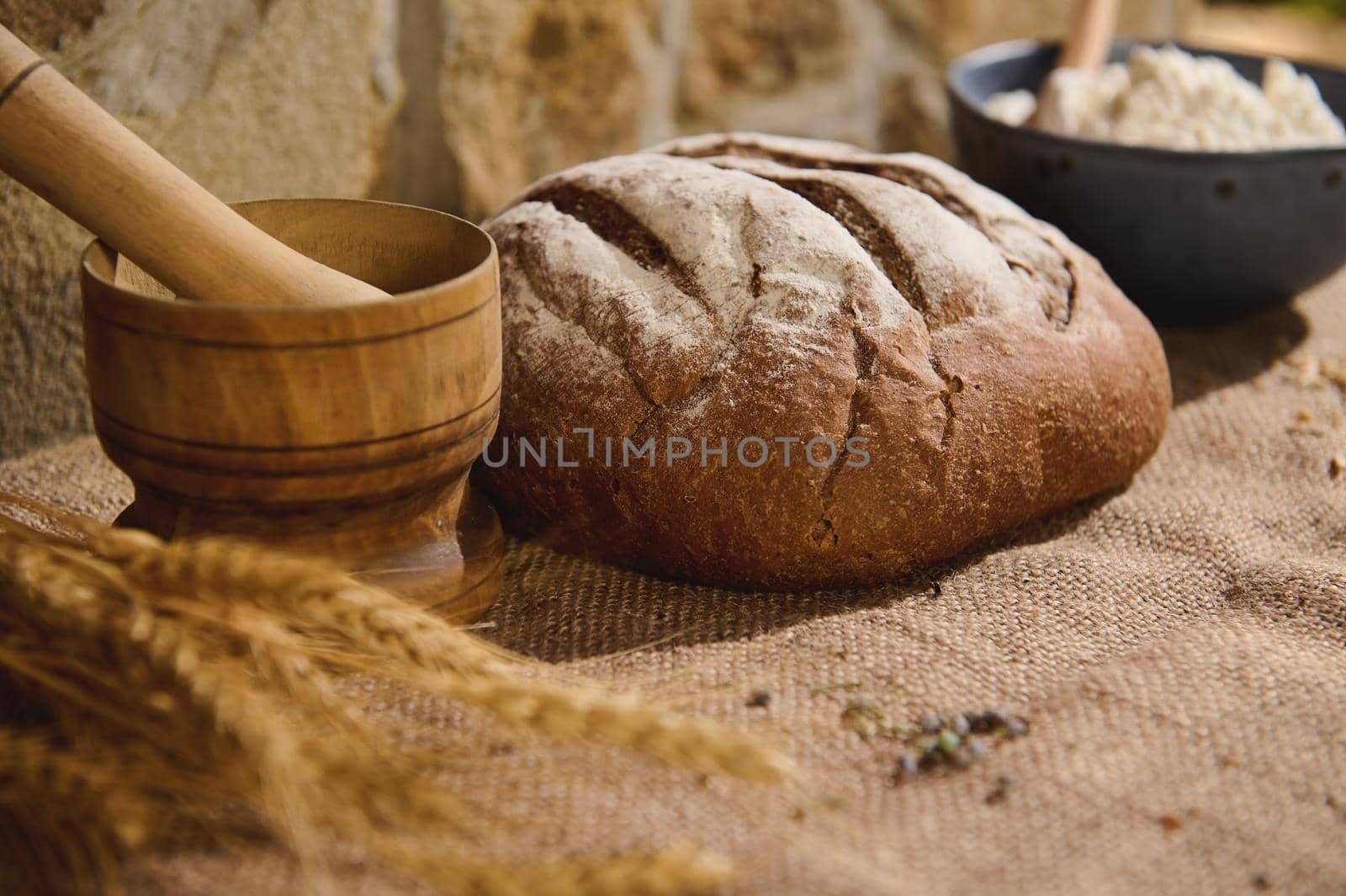 Still life. Traditional homemade wholesome sourdough wheaten bread, a wooden mortar and wheat spikelets on the sacklock by artgf