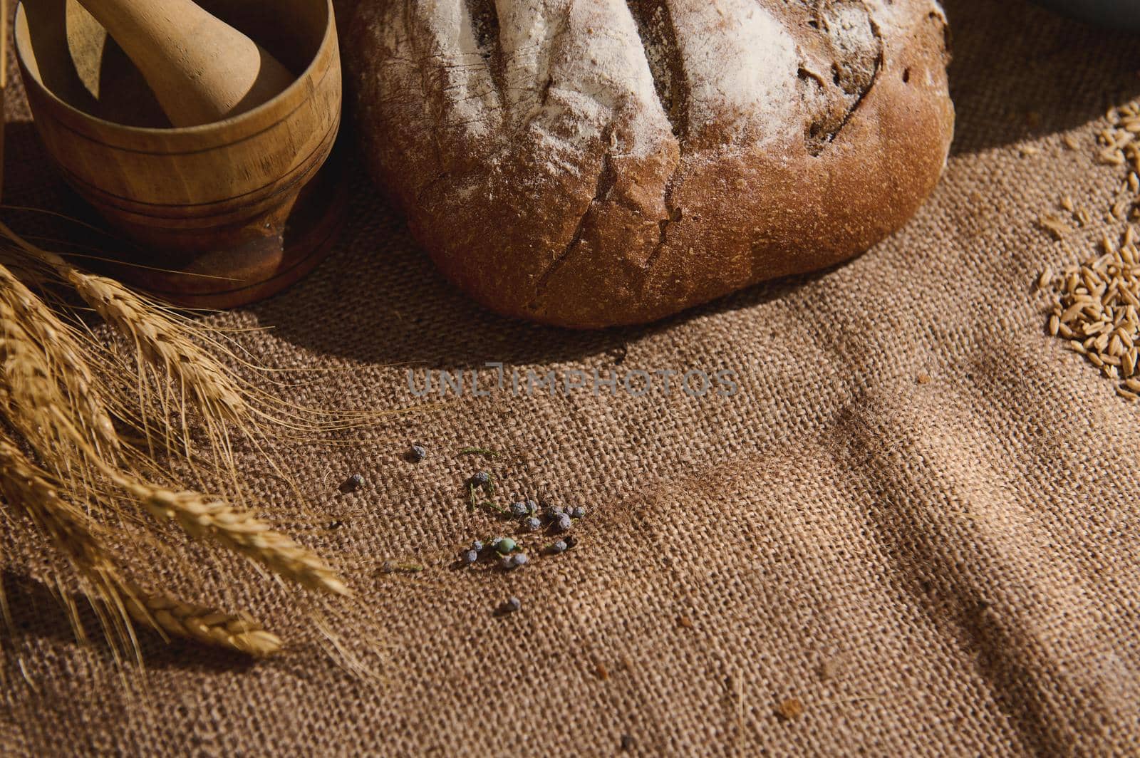 Top view. Traditional wholesome sourdough wheaten bread, on a linen tablecloth next to a wooden mortar and ears of wheat by artgf