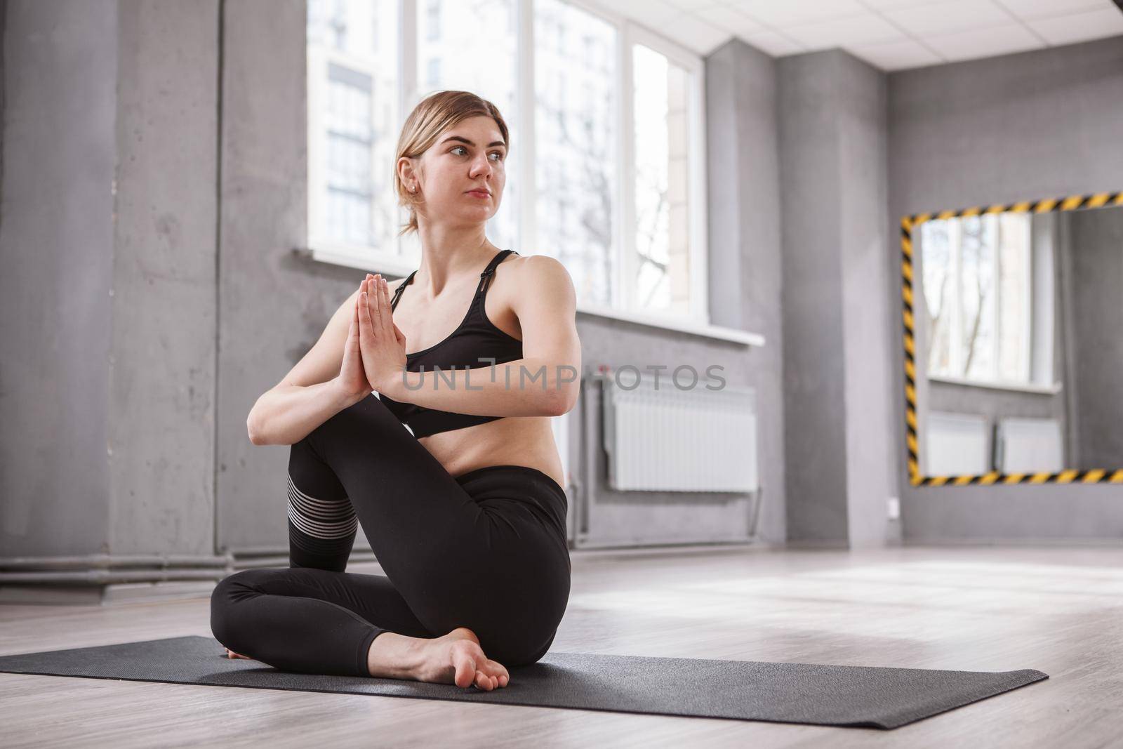 Young lovely woman practicing yoga at gym studio, holding hands in namaste gesture, copy space