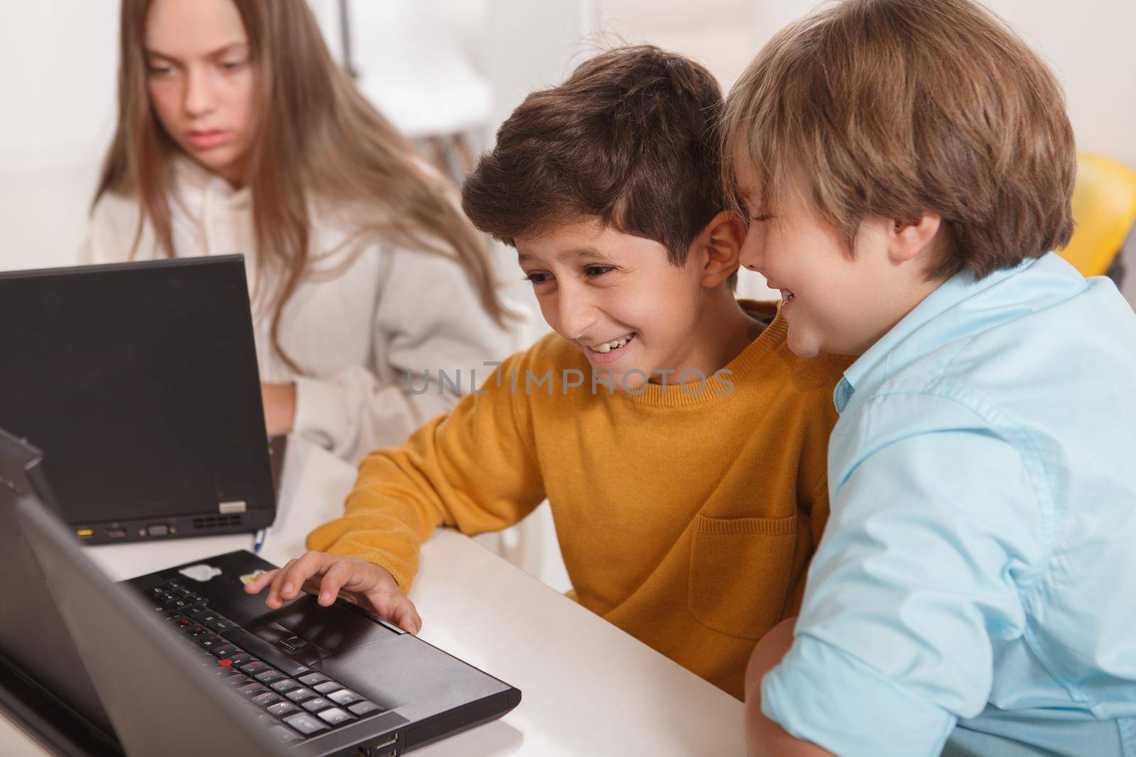 Cute little boys laughing, having fun studying together, using laptop