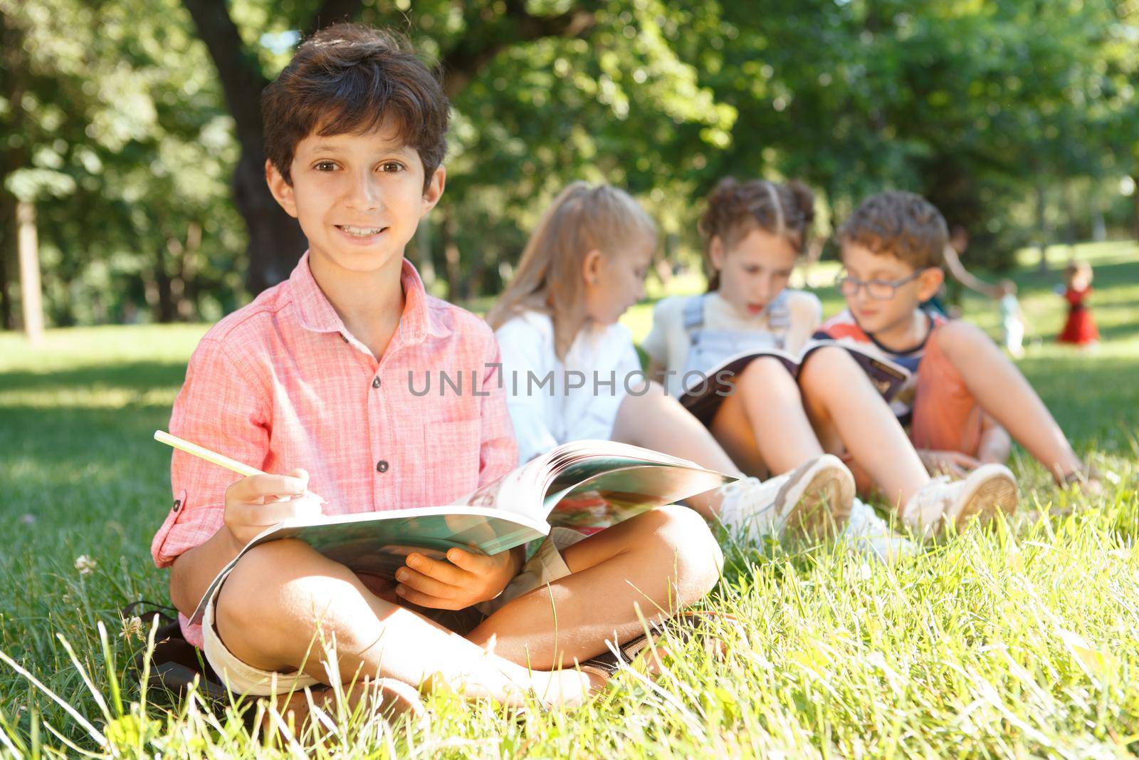 Happy charming little boy smiling to the camera while studying outdoors with his classmates