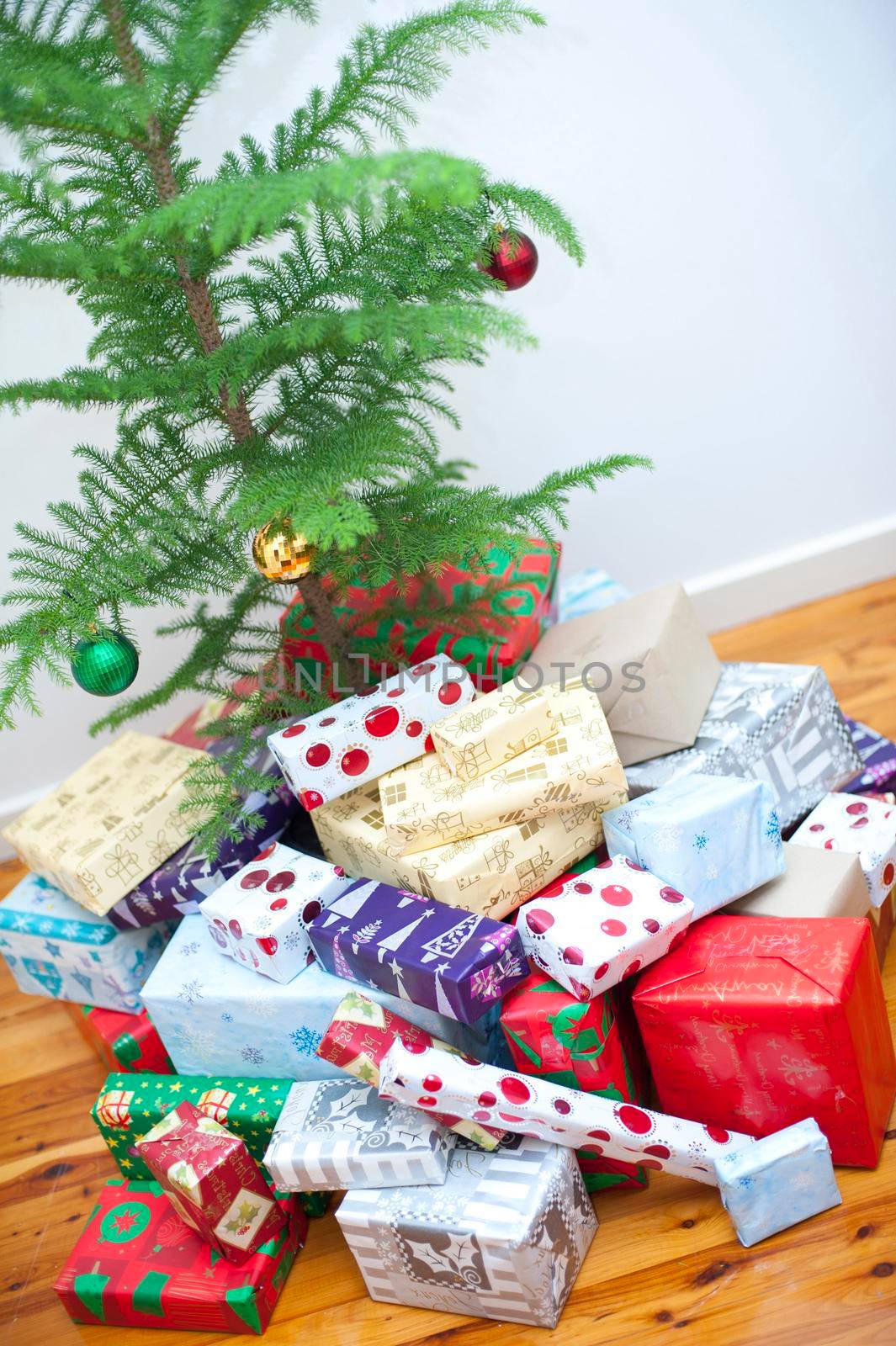 Large collection of colourful gift-wrapped Xmas presents gathered at the foot of the Christmas tree ready for a family celebration