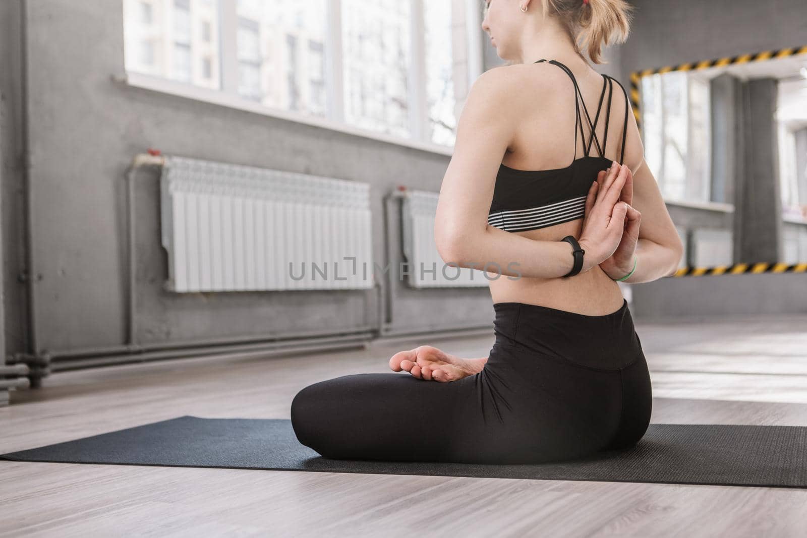 Cropped rear view shot of a woman sitting in lotus asana at sport studio, copy space
