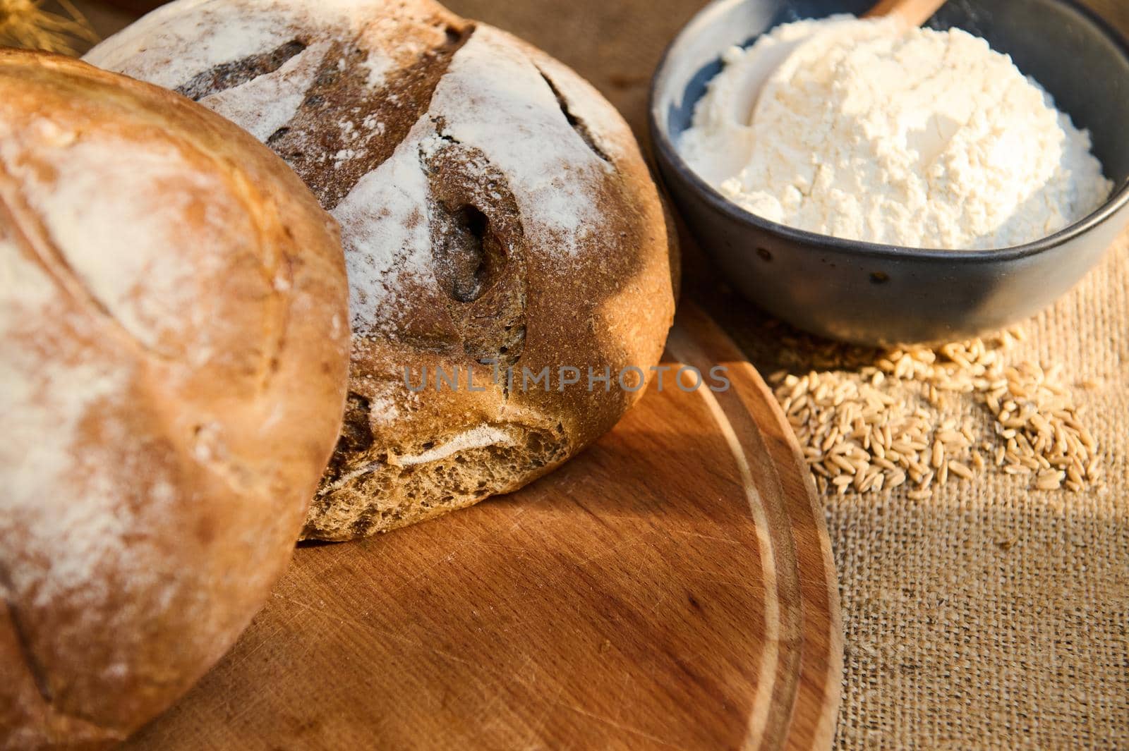 Cropped view of loaves of round freshly baked rustic whole grain bread and wheat ears on a wooden backdrop. Pastries by artgf