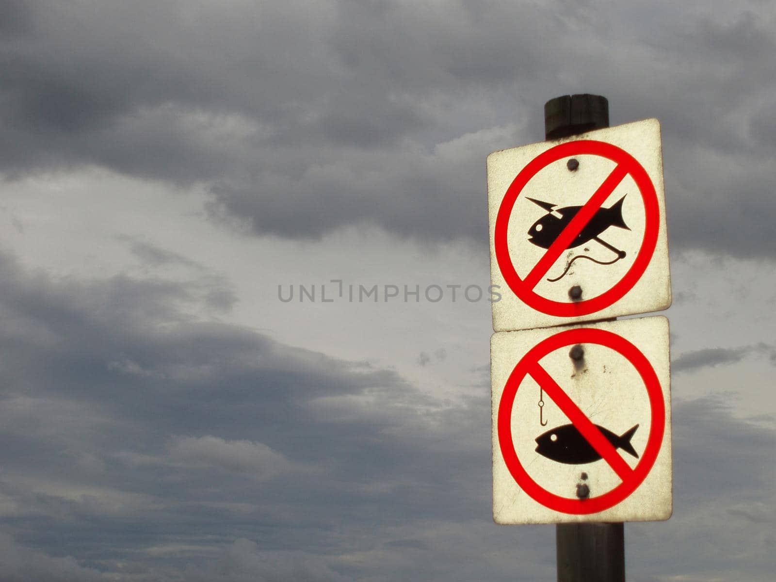 two signs marking a no fishing area against a backdrop of storm clouds