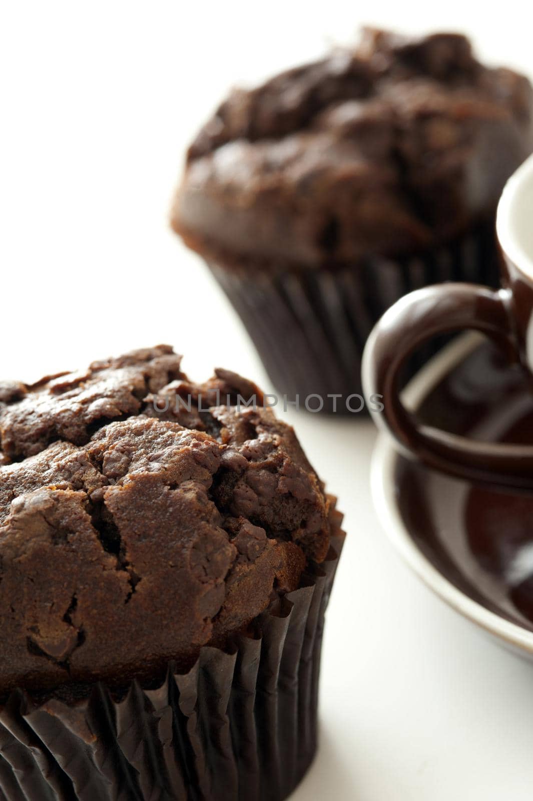Dark brown freshly baked chocolate muffin served with a cup of tea of coffee, close up partial views of the cookie and cup
