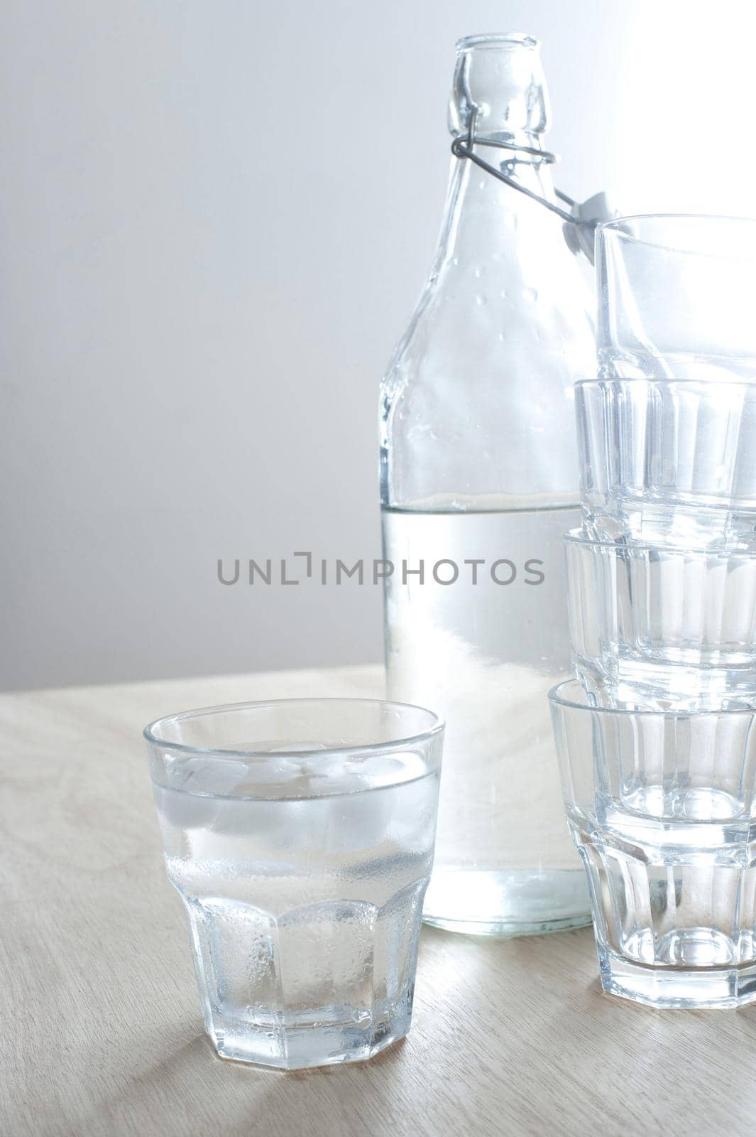 Refreshing cold pure water served in a glass bottle with one full tumbler and a stack of empty glasses alongside, healthy drink with copyspace