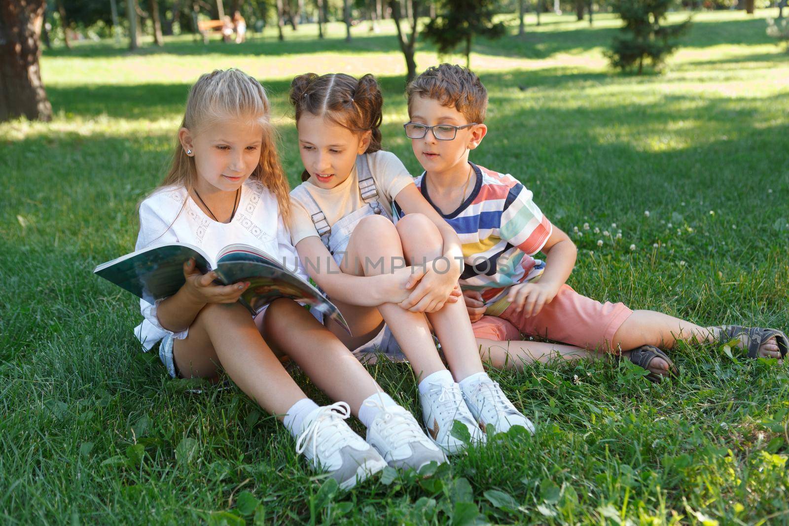 Three children reading a book together on the grass at the park