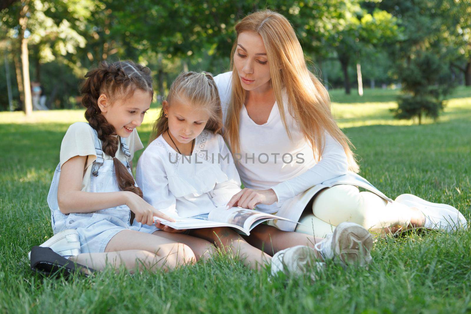 Two little girls enjoying open air lesson in the park with their favorite teacher