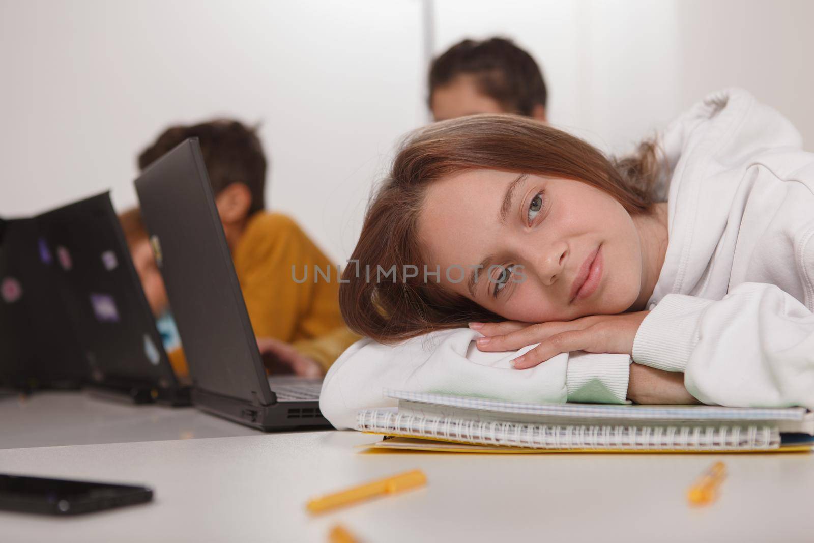 Close up of a lovely teenage girl resting on her textbooks, looking away dreamily sitting at classroom