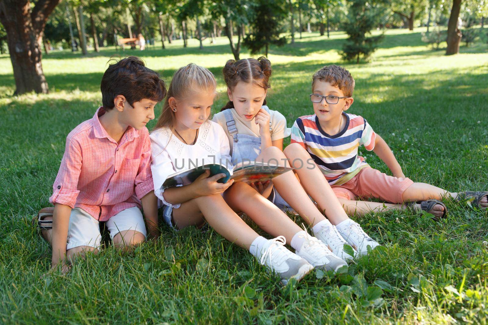 Group of kids reading a book together outdoors in the park