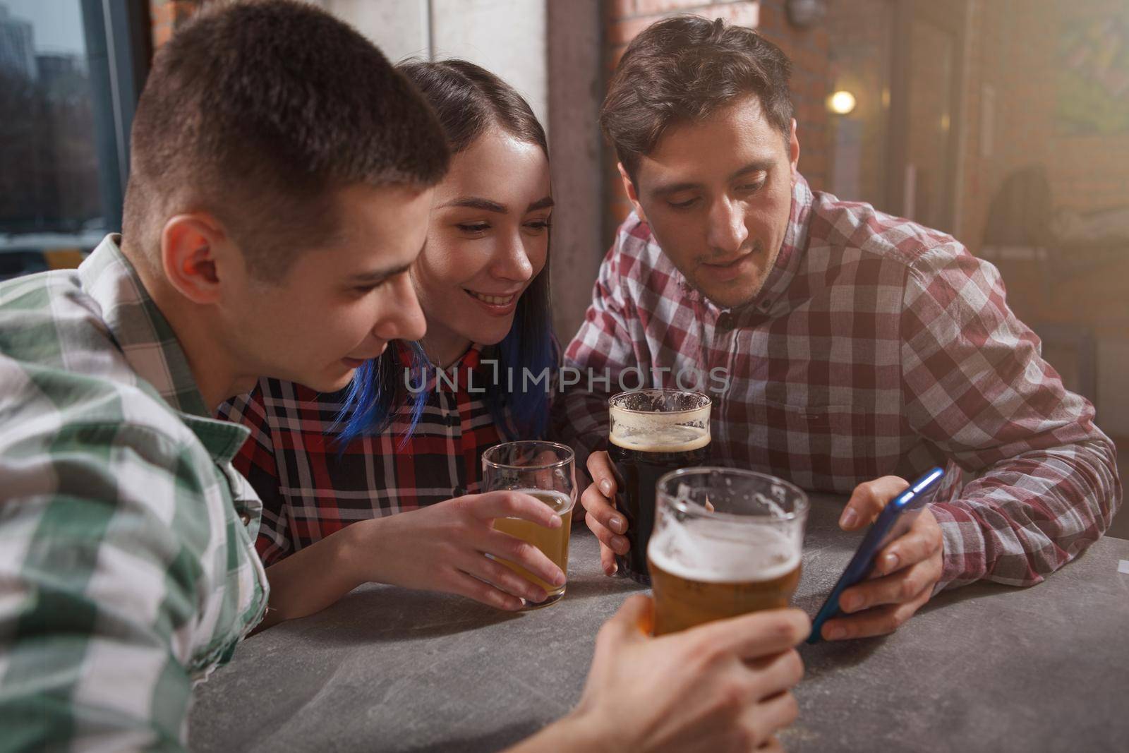 Group of friends watching something on smart phone, drinking beer together at the pub
