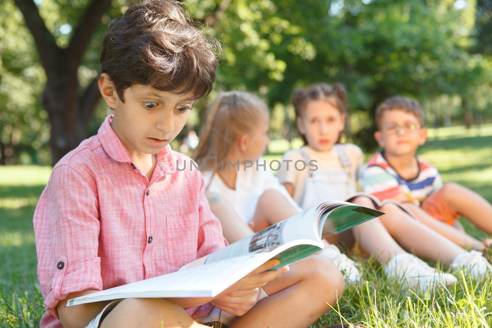 Cute little boy looking overwhelmed, reading a book at public park