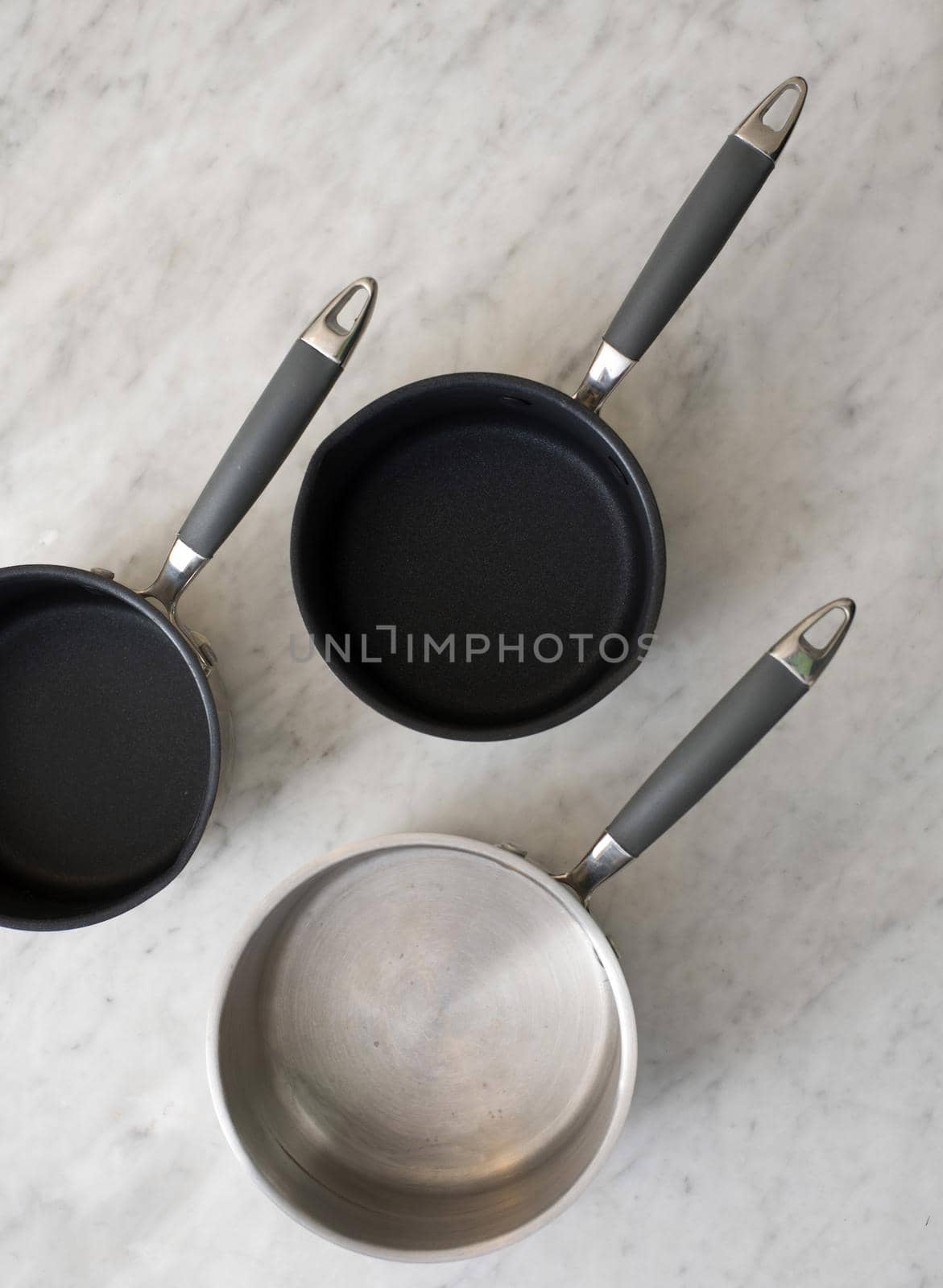 Three empty clean metal pots or saucepans viewed from above on a mottled grey surface in a food and cookery concept