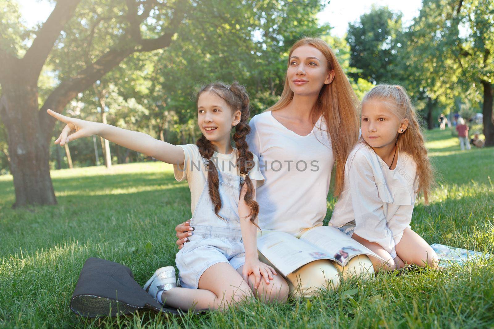 Cheerful female teacher relaxing at the park on the grass with her students two schoolgirls