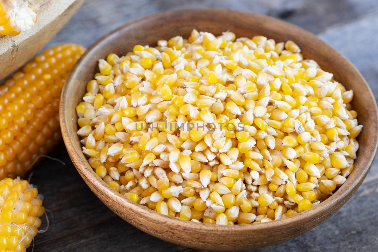 Popcorn kernels in a wooden bowl with popcorn on the cob