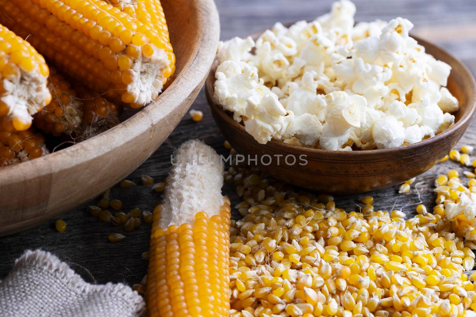Harvesting popcorn from the cob with a bowl of popped corn surrounded by kernels and cob with kernels partially removed.